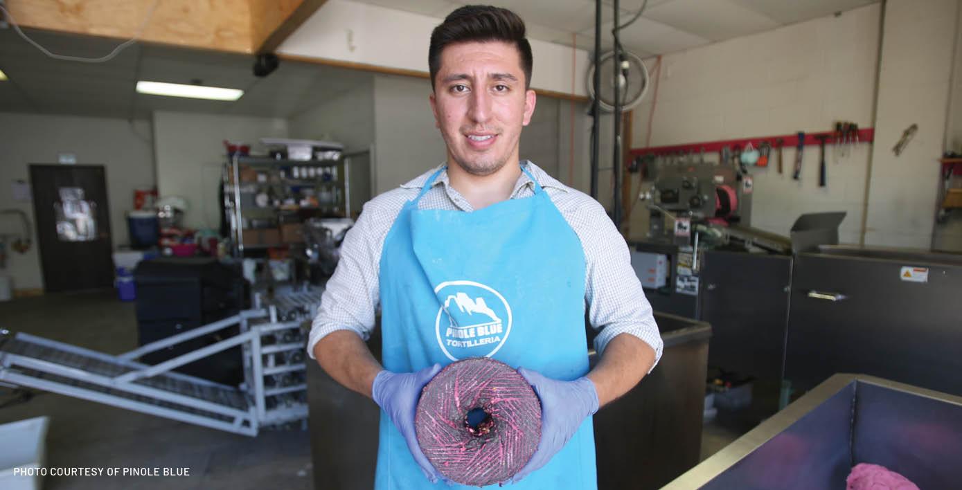 The founder, Eddie Sandoval, a hispanic male, holding a volcanic stone, used to grind corn.